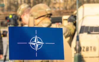 Flag and symbol of NATO, North Atlantic Treaty Organization, force integration unit with out of focus soldiers with helmets and military vehicles