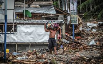 TOPSHOT - A resident carrying belongings walks amongst debris from landslide in the landslide-hit village of Kusiong in Datu Odin Sinsuat in the southern Philippines' Maguindanao province on October 29, 2022. - Severe Tropical Storm Nalgae whipped the Philippines on October 29 after unleashing flash floods and landslides that officials said left at least 45 people dead. (Photo by Ferdinandh CABRERA / AFP) (Photo by FERDINANDH CABRERA/AFP via Getty Images)