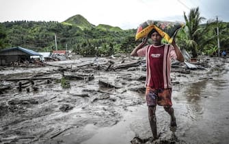 A resident carrying a sack of rice walks along a muddied road next to destroyed house in the landslide-hit village of Kusiong in Datu Odin Sinsuat in the southern Philippines' Maguindanao province on October 29, 2022. - Severe Tropical Storm Nalgae whipped the Philippines on October 29 after unleashing flash floods and landslides that officials said left at least 45 people dead.  (Photo by Ferdinandh CABRERA / AFP) (Photo by FERDINANDH CABRERA / AFP via Getty Images)
