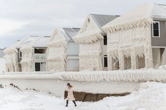 TOPSHOT - A person walks by homes covered in ice at the waterfront community of Crystal Beach in Fort Erie, Ontario, Canada, on December 28, 2022, following a massive snow storm that knocked out power in the area to thousands of residents.  (Photo by Cole Burston/AFP) (Photo by COLE BURSTON/AFP via Getty Images)