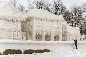 A person takes photos of a scene of frozen houses in the waterfront community of Crystal Beach in Fort Erie, Ontario, Canada, on December 28, 2022, following a massive snow storm that knocked out power in the area to thousands of residents. (Photo by Cole Burston / AFP) (Photo by COLE BURSTON/AFP via Getty Images)