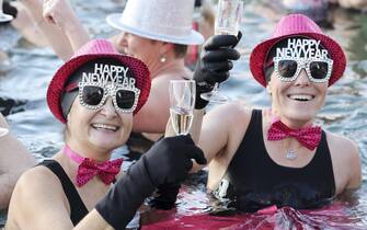 epa10385284 People toast with champagne while swimming in the cold water during the New Year's traditional swimming in the Lake of Geneva at the Bains des Paquis, in Geneva, Switzerland, 01 January 2023.  EPA/SALVATORE DI NOLFI