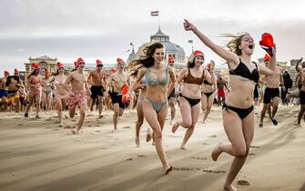 epa10385224 People run into the sea at the beach of Scheveningen on New Year's Day, Scheveningen, Netherlands, 01 January 2023. The traditional New Year's dive was resumed after the two previous editions were canceled due to the corona crisis.  EPA/REMKO DE WAAL