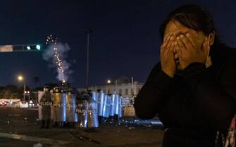 1246491865 LIMA, PERU - JANUARY 23: A woman covers her eyes as a police officer fires tear gas. Thousands of people protested in a new day of demonstrations against the government of Peruvian President Dina Boluarte in Lima, Peru on January 23, 2023. The protesters demanded general elections, the removal of President Boluarte and justice for protesters killed during clashes with the police, during the recent political crisis. The massive demonstration took place after the news broke that Boluarte tried to resign on two occasions, but that his Prime Minister, Alberto Otarola, would have convinced her not to do so, because otherwise they could pay for crimes against humanity with up to 20 years in prison. (Photo by Lucas Aguayo Araos/Anadolu Agency via Getty Images)