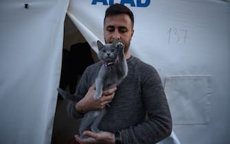 KAHRAMANMARAS, TURKIYE - FEBRUARY 24: Ugur Tamer Keklik, an earthquake survivor lives the tent city established in Vali Saim Cotur Stadium and around with his cat named "Miya" after 7.7 and 7.6 magnitude earthquakes hit multiple provinces of Turkiye including Kahramanmaras on February 24, 2023. Some survivors of earthquakes in Kahramanmaras live together in a tent city with their animals, such as fish, birds, partridges, cats and dogs, which they rescued while leaving their homes. Established by the Sakarya 7th Commando Brigade Command, the tent city hosts nearly 3,500 earthquake victims as well as dozens of pets. (Photo by Fatih Kurt/Anadolu Agency via Getty Images)