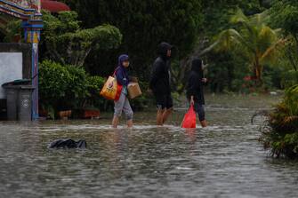 epa10501685 Residents walk through flood waters in the rain after some areas in Johor state were affected by flooding, in Yong Peng, Johor, Malaysia, 04 March 2023. According to state media, more than 33,000 people were evacuated in four states affected by the flooding.  EPA/FAZRY ISMAIL