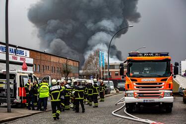 epa10566219 Firefighters gather at the scene of a fire burning at a warehouse in the Rothenburgsort district of Hamburg, Germany, 09 April 2023. Residents have been warned of heavy smoke and possible toxins in the air. An alert issued by the Hamburg fire department said smoke gasses and chemical components in the air could affect breathing.  EPA/DOMINICK WALDECK
