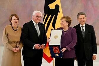 epa10577242 Former German Chancellor Angela Merkel (2-R) holds the box with the 'Grand Cross of the Order of Merit of the Federal Republic of Germany' as she poses for the media with her husband Joachim Sauer (R), German President Frank- Walter Steinmeier (2-L) and his wife Elke Buedenbender (L) after the awarding ceremony n Berlin, Germany, April 17, 2023. EPA/FILIP SINGER