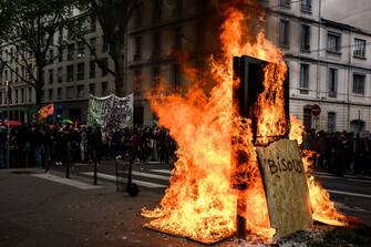 Protesters take part in a demonstration next to a burning advertisment pannel and a wooden board reading "kisses" on May Day (Labour Day), to mark the international day of workers, more than a month after the government pushed an unpopular pensions reform act through parliament, in Lyon, eastern France, on May 1, 2023. - Opposition parties and trade unions have urged protesters to maintain their three-month campaign against the law that will hike the retirement age to 64 from 62. (Photo by JEFF PACHOUD / AFP) (Photo by JEFF PACHOUD/AFP via Getty Images)