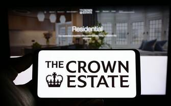 Person holding cellphone with logo of British statutory corporation Crown Estate on screen in front of business webpage. Focus on phone display.