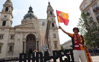 epa10662859 A fan of Roma poses for a photo with a replica of the UEFA Europa League Trophy in front of the St. Stephen's Basilica in Budapest, Hungary, 30 May 2023. AS Roma will face Sevilla FC in the UEFA Europa League final at the Puskas Arena in Budapest on 31 May 2023.  EPA/ANNA SZILAGYI