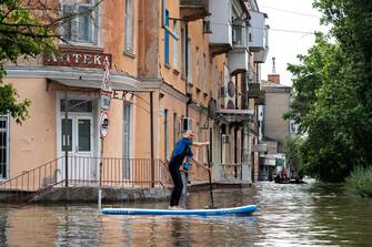 A local resident sails on a sup board during an evacuation from a flooded area in Kherson on June 8, 2023, following damages sustained at Kakhovka hydroelectric power plant dam. Ukrainian President Volodymyr Zelensky visited the region flooded by the breached Kakhovka dam Thursday, as the regional governor said 600 square kilometres were underwater. (Photo by ALEKSEY FILIPPOV / AFP)