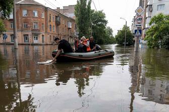 Volunteers carry local residents on an inflatable boat during an evacuation from a flooded area in Kherson on June 8, 2023, following damages sustained at Kakhovka hydroelectric power plant dam. Ukrainian President Volodymyr Zelensky visited the region flooded by the breached Kakhovka dam on June 8, 2023, as the regional governor said 600 square kilometres were underwater. (Photo by ALEKSEY FILIPPOV / AFP)
