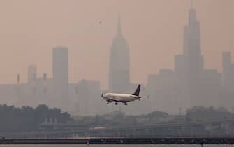 epa10680359 An airplane lands at LaGuardia airport with buildings in Manhattan skyline in the background as smoke from wildfires burning in Canada continues to create unhealthy air quality conditions in New York, New York, USA, 08 June 2023. New York City continues to be under an air quality alert as result of the smoke, which is affecting large portions of the United States and causing flight delays around as well as ground stops due to poor visibility.  EPA/JUSTIN LANE