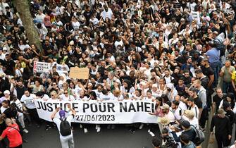 Attendees hold a banner reading "Justice for Nahel", during a commemoration march for a teenage driver shot dead by a policeman, in the Parisian suburb of Nanterre, on June 29, 2023. Violent protests broke out in France in the early hours of June 29, 2023, as anger grows over the police killing of a teenager, with security forces arresting 150 people in the chaos that saw balaclava-clad protesters burning cars and setting off fireworks. Nahel M., 17, was shot in the chest at point-blank range in Nanterre in the morning of June 27, 2023, in an incident that has reignited debate in France about police tactics long criticised by rights groups over the treatment of people in low-income suburbs, particularly ethnic minorities. (Photo by Bertrand GUAY / AFP)