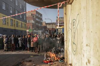 EDITORS NOTE: Graphic content / TOPSHOT - People standing at a bonfire look on as unseen firefighters work at the scene of a fire in a building in Johannesburg on August 31, 2023. At least 20 people have died and more than 40 were injured in a fire that engulfed a five-storey building in central Johannesburg on August 31, 2023, the South African city's emergency services said.  (Photo by Michele Spatari / AFP) (Photo by MICHELE SPATARI/AFP via Getty Images)