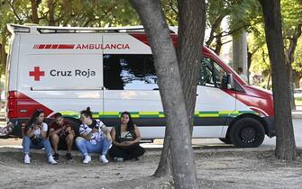 Four people sit next to an ambulance outside the city's Sports Pavillion where relatives and friends of the victims killed in a fire at a nightclub in Murcia, have received psychological assistance on October 1, 2023. At least 13 people were killed in a fire in a Spanish nightclub today morning, authorities said, with fears the toll could still rise as rescue workers sift through the debris. The fire appears to have broken out in a building housing the "Teatre" and "Fonda Milagros" clubs in the city of Murcia in southeastern Spain in the early morning hours. (Photo by JOSE JORDAN / AFP) (Photo by JOSE JORDAN/AFP via Getty Images)