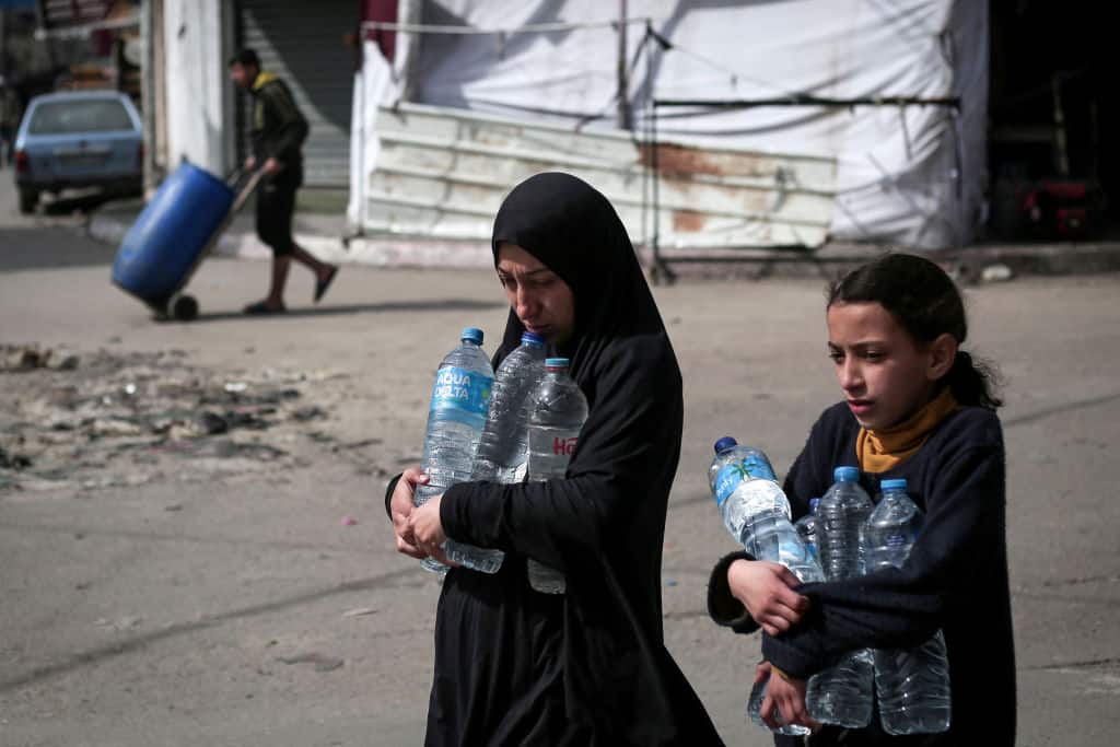 Due donne palestinesi portano bottiglie d'acqua a Rafah.