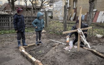 BUCHA, KYIV PROVINCE, UKRAINE, APRIL 04: A young kid gives an offering of food to his mother grave as his younger brother and a neighbor stand next to it, in the town of Bucha, on the outskirts of Kyiv, after the Ukrainian army secured the area following the withdrawal of the Russian army from the Kyiv region on previous days, Bucha, Ukraine, April 4th, 2022. (Photo by Narciso Contreras/Anadolu Agency via Getty Images)