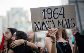 EDITORS NOTE: Graphic content / A woman holds a sign reading "1964 never again", during a demonstration at Cinelandia square in Rio de Janeiro, Brazil on March 31, 2019, to protest against the commemoration of the 55th anniversary of the coup that established more than two decades of military rule. - Thousands of protesters took to the streets of Brazil for the 55th anniversary of the coup, the protests were sparked by the order recently issued by far-right President Jair Bolsonaro for defense forces to "appropriately" commemorate the overthrow of President Joao Goulart. (Photo by Daniel RAMALHO / AFP)        (Photo credit should read DANIEL RAMALHO/AFP via Getty Images)