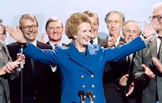 British Prime Minister Margaret Thatcher acknowledges applauds on Ocotber 13, 1989 at the end of the Conservative Party conference in Blackpool. At left Foreign Secretary John Major and at right Home Secretary John Hurt.        (Photo credit should read JOHNNY EGGITT/AFP via Getty Images)