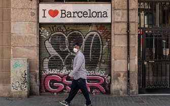 BARCELONA, SPAIN - MAY 06: A man wearing a protective face mask walk past a closed souvenir shop on May 06, 2020 in Barcelona, Spain. Despite of small businesses are allowed to open since last Monday, many shops and restaurants remain closed. Spain is opening businesses such as hairdressers, delivery food restaurants and book shops after weeks of lockdown. Spain has had more than 218,000 confirmed cases of COVID-19 and over 25,000 reported deaths, although the rate has declined due to lockdown measures. (Photo by David Ramos/Getty Images)