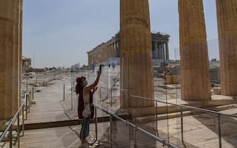 A worker wearing a protective mask cleans a divider made of plexiglass at the entrance of the Acropolis in Athens on May 18, 2020 amid the pandemic of the novel coronavirus (COVID-19). - Greece reopened the Acropolis in Athens and all open-air archaeological sites in the country to the public on May 11 after a two-month closure due to the coronavirus pandemic. (Photo by Aris MESSINIS / AFP) (Photo by ARIS MESSINIS/AFP via Getty Images)