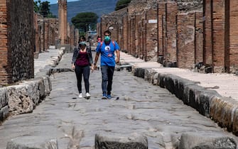 Visitors wearing a face mask walk across the archeological site of Pompeii on May 26, 2020, as the country eases its lockdown aimed at curbing the spread of the COVID-19 infection, caused by the novel coronavirus. - Italy's world-famous archeological site Pompeii reopened to the public on May 26,bBut with foreign tourists still prohibited from travel to Italy until June, the site that attracted just under 4 million visitors in 2019 is hoping that for now, Italian tourists can make up at least a fraction of the difference. (Photo by Tiziana FABI / AFP) (Photo by TIZIANA FABI/AFP via Getty Images)