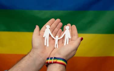 hands of man with gay paper family on lgtb rainbow flag background