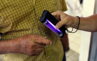 A man holds out his hand as an electoral worker scans it with an ultraviolet light to verify he had not already voted during the referendum for Puerto Rico political status at a polling station in Guaynabo, on June 11, 2017. / AFP PHOTO / Ricardo ARDUENGO        (Photo credit should read RICARDO ARDUENGO/AFP via Getty Images)
