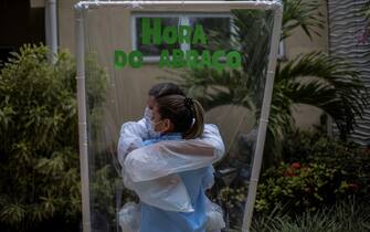 Due operatrici sanitarie brasiliane impegnate nell'emergenza Covid si abbracciano attraverso una pellicola protettiva durante un momento di pausa