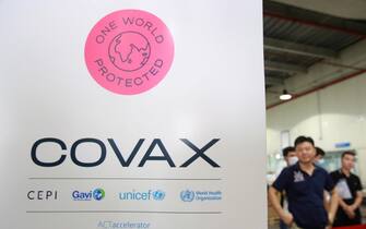 epa09109888 People stand next to a COVAX sign at Noi Bai international airport in Hanoi, Vietnam, 01 April 2021. Vietnam has received the first batch of AstraZeneca/Vaxzevira vaccine through Covax initiative on 01 April 2021.  EPA/LUONG THAI LINH