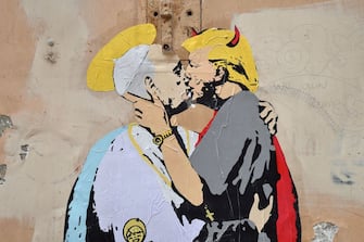 A collage shows Pope Francis kissing US President Donald Trump with a caption by Italian artist TvBoy reading in English and Italian "The Good forgives the Evil" in tiny letters along Francis belt, on May 11, 2017 near Castel Sant'Angelo in central Rome.  / AFP PHOTO / Andreas SOLARO / RESTRICTED TO EDITORIAL USE - MANDATORY MENTION OF THE ARTIST UPON PUBLICATION - TO ILLUSTRATE THE EVENT AS SPECIFIED IN THE CAPTION        (Photo credit should read ANDREAS SOLARO/AFP via Getty Images)