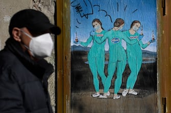 TOPSHOT - A man wearing face mask walks by a new work by Italian street artist TvBoy named "The three Vaccines" depicting The Three Graces painting by Italian painter Raphael, in Barcelona on January 19, 2021. (Photo by Josep LAGO / AFP) / RESTRICTED TO EDITORIAL USE - MANDATORY MENTION OF THE ARTIST UPON PUBLICATION - TO ILLUSTRATE THE EVENT AS SPECIFIED IN THE CAPTION (Photo by JOSEP LAGO/AFP via Getty Images)