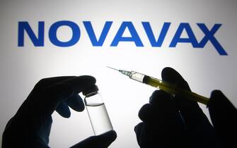 UKRAINE - 2021/04/27: In this photo illustration, silhouette of hands in medical gloves hold a medical syringe and a vial in front of Novavax logo. (Photo Illustration by Pavlo Gonchar/SOPA Images/LightRocket via Getty Images)