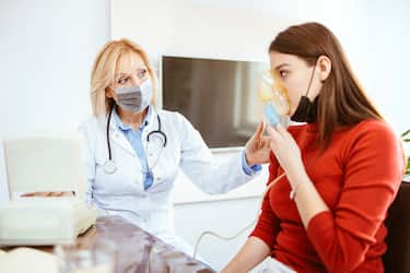 Female doctor applying medicine inhalation treatment on a young woman in doctor's office. Hard breathing due to asthma or allergies.
