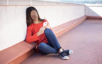 Chica adolescente mirando el smartphone sentada en la azotea
