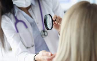Dermatologist examines patient's face through magnifying glass. Facial skin problems psychosomatics concept