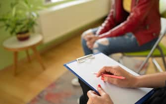 Close up of a psychologist notes and a students knees during a mental health meeting in a stylish office