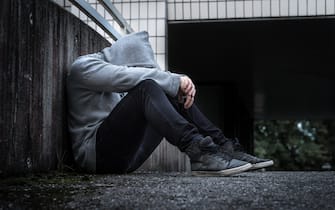 Depression, social isolation, loneliness, mental health and discrimination concept. Sad, lonely, depressed and unhappy man. Hooded person sitting.