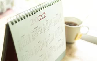 Paper desktop calendar 2022 schedule with tea cup on wooden desk