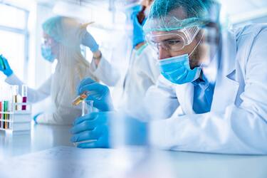 Concentrated mid adult chemist working with poisonous liquid in laboratory. His colleagues are in the background.