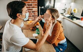 Couple cleaning hands with hand sanitiser, wearing n95 face mask