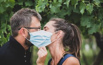 Couple of lovers kissing behind the protective mask - new normal lifestyle concept with the couple in love outdoor kiss - love and corona virus