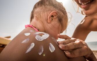 Close up of a mother applying moisturizer on her daughter's shoulder while spending a summer day on the beach.