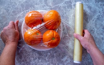 Woman is holding packaged orange fruits in hand. Using food film for fruits storage in fridge. Food storage concept.