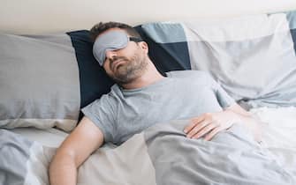 Man portrait in bed wearing sleeping eye mask feeling comfortable