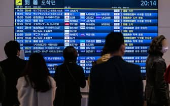 People wait in front a board showing international flight arrivals at Tokyo's Haneda international airport on December 28, 2022. - Hong Kong authorities on December 28 asked Japan to remove restrictions on direct flights from the city, which were imposed following the explosion of coronavirus cases in mainland China. (Photo by Philip FONG / AFP) (Photo by PHILIP FONG/AFP via Getty Images)