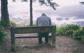 Sad and lonely man sitting on bench overlooking sea on Vancouver Island