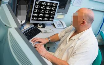 Senior radiologist of Oncology institute is examing MRI and CAT scans of human abdomen on his monitors